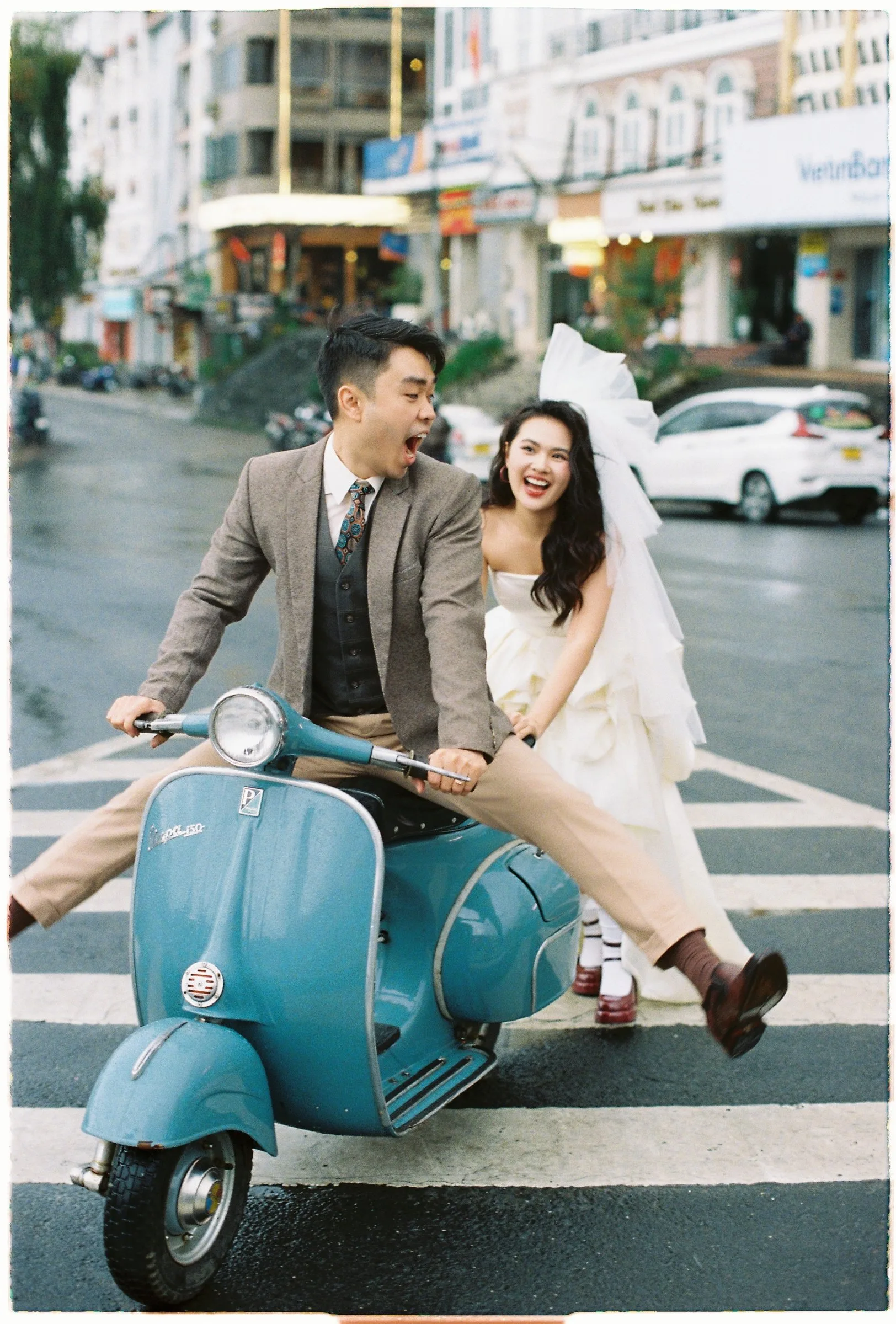 Couple laughing on a vintage Vespa in the streets of Da Lat, pre-wedding on film