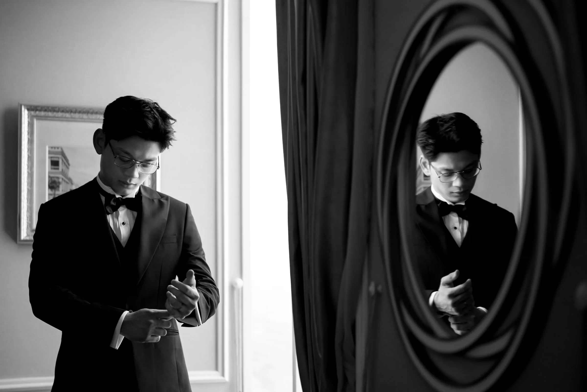 Black and white portrait of the groom fastening his cufflinks before a Da Nang wedding