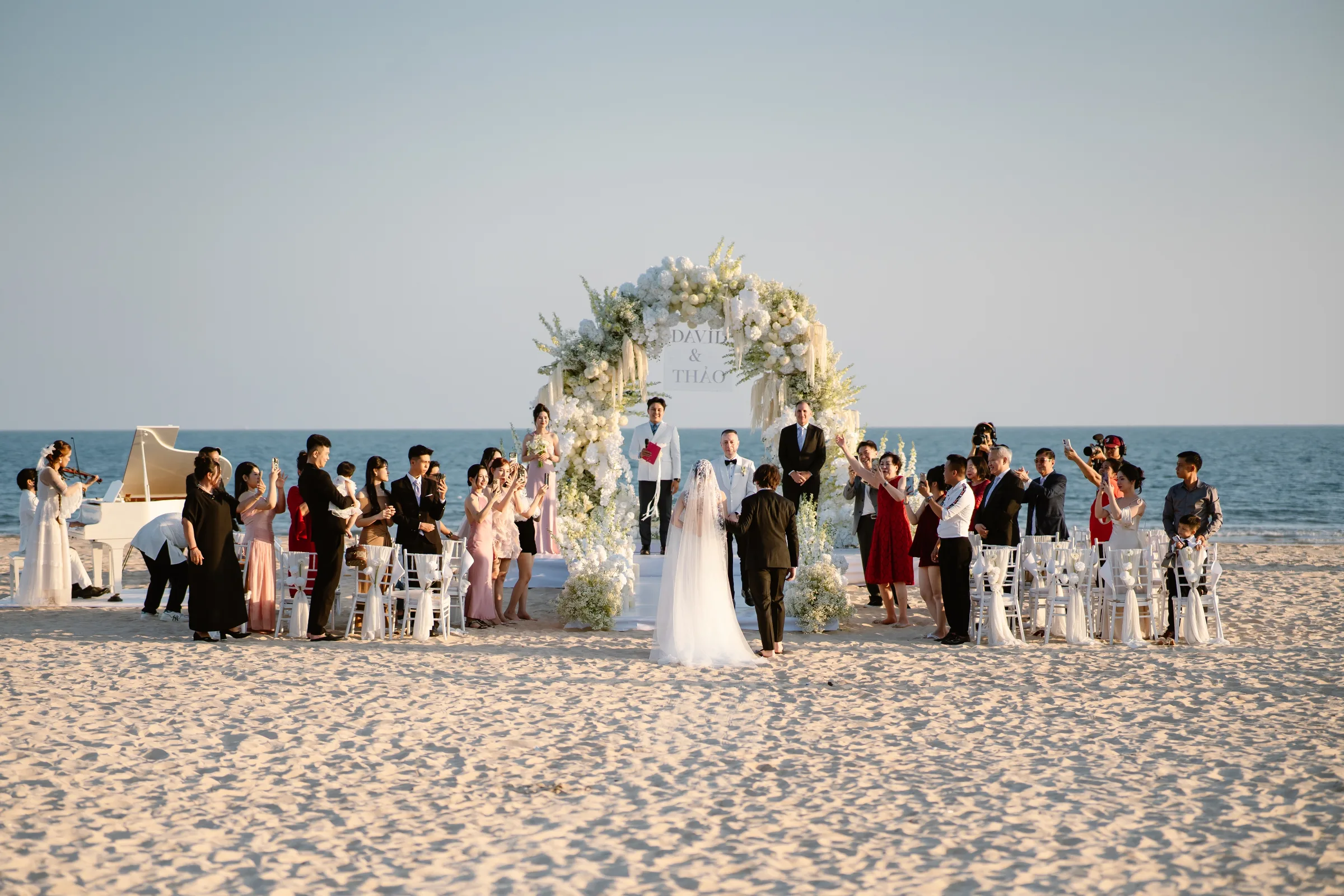 Beachfront wedding ceremony with a white piano and floral arch at Melia Ho Tram, Vietnam
