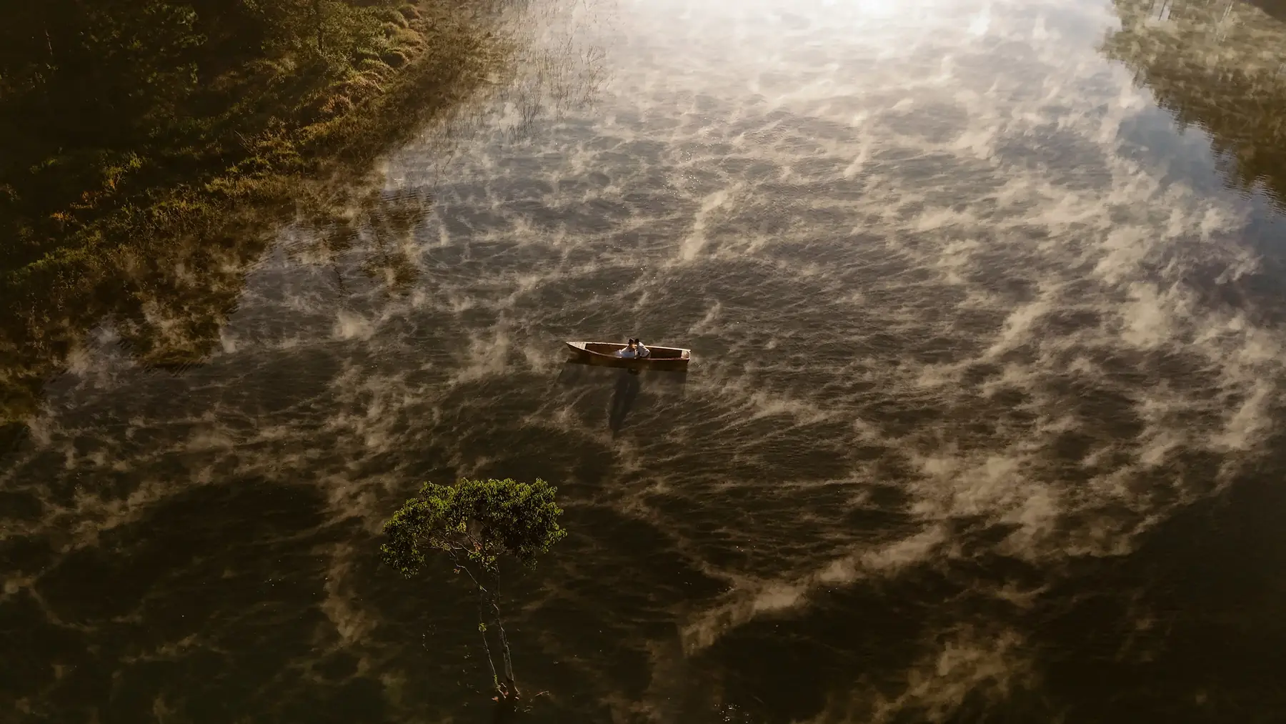 Aerial view of a couple in a wooden boat on a misty Da Lat lake at dawn